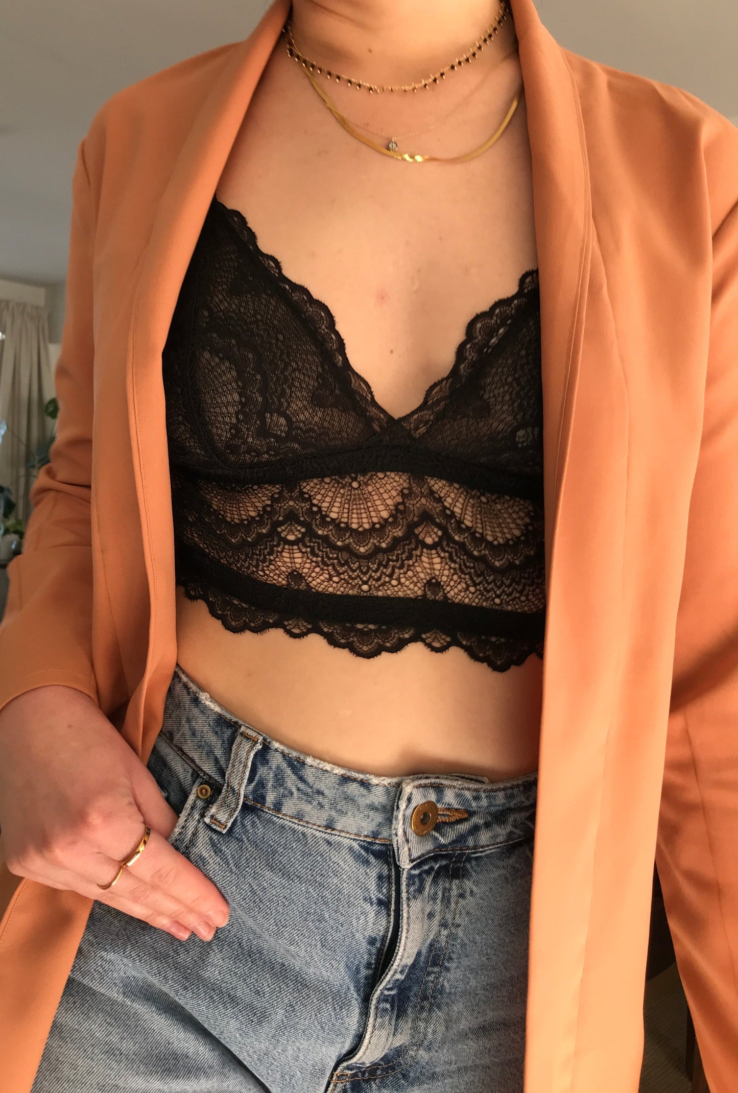 Person wearing a peach blouse with a black lace bralette underneath, standing indoors.