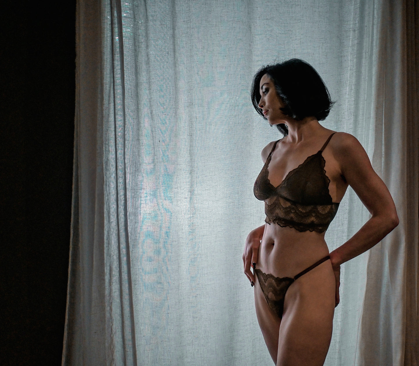 Woman wearing a lace lingerie set in front of a sheer curtain
