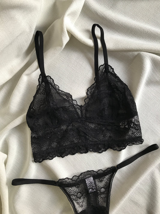A black lace bralette with adjustable straps and a matching pair of briefs, laid flat on a white background.