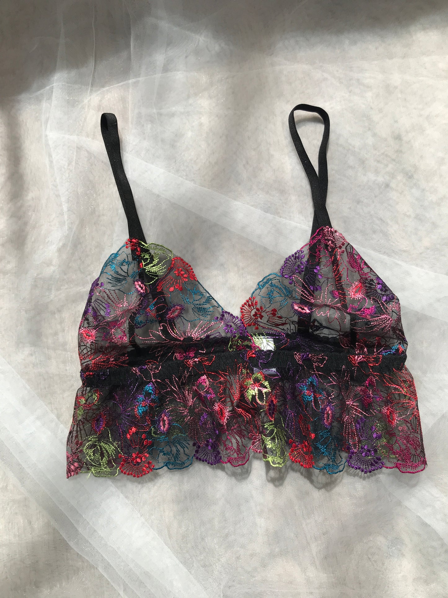 A frilly bralette with floral patterns in multicolor, predominantly pink and black, displayed on a flat surface.