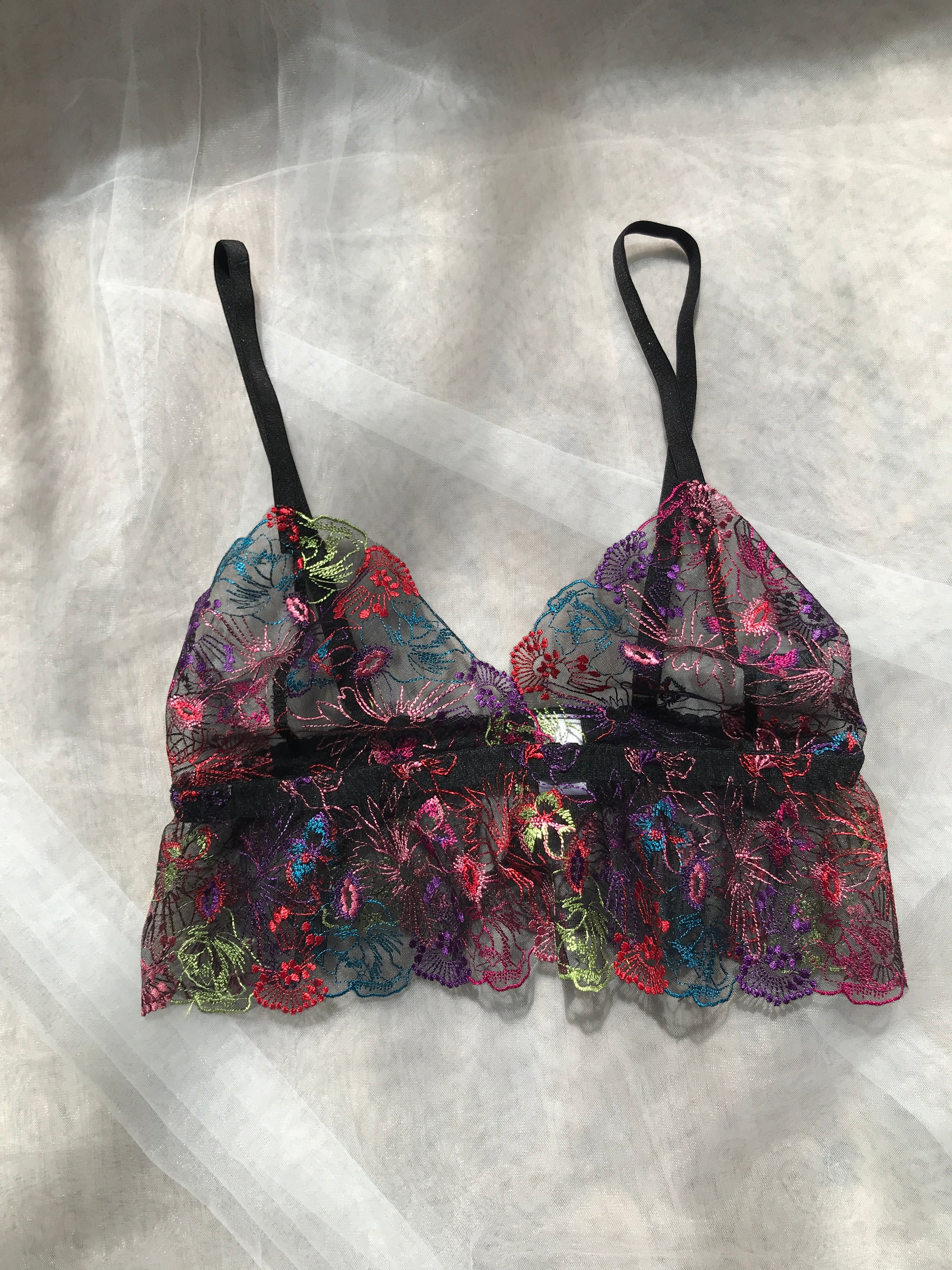 A frilly bralette with floral patterns in multicolor, predominantly pink and black, displayed on a flat surface.
