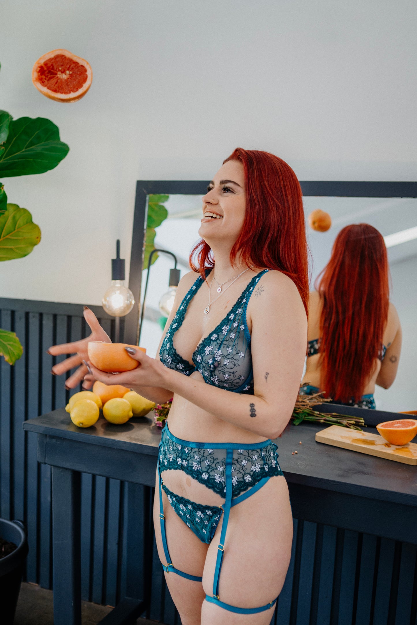 This image features a woman modeling the Jade G-String, which is presented against a backdrop of a modern kitchen setting. The woman is wearing the G-string, which is prominently displayed, along with a few other pieces of intimate apparel, such as a bra and a garter belt, which are also visible in the background.
