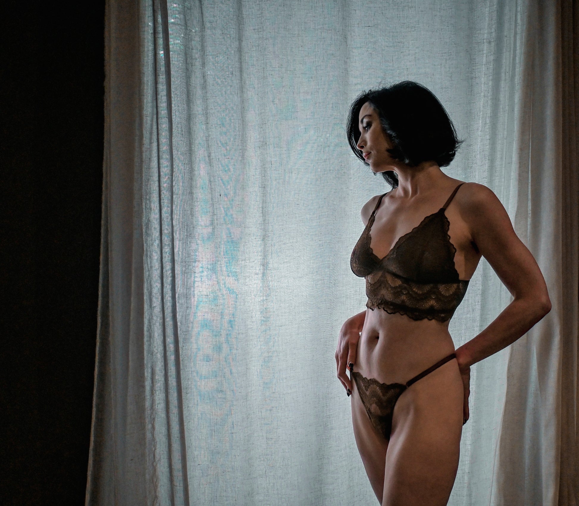 Woman wearing a lace lingerie set in front of a sheer curtain