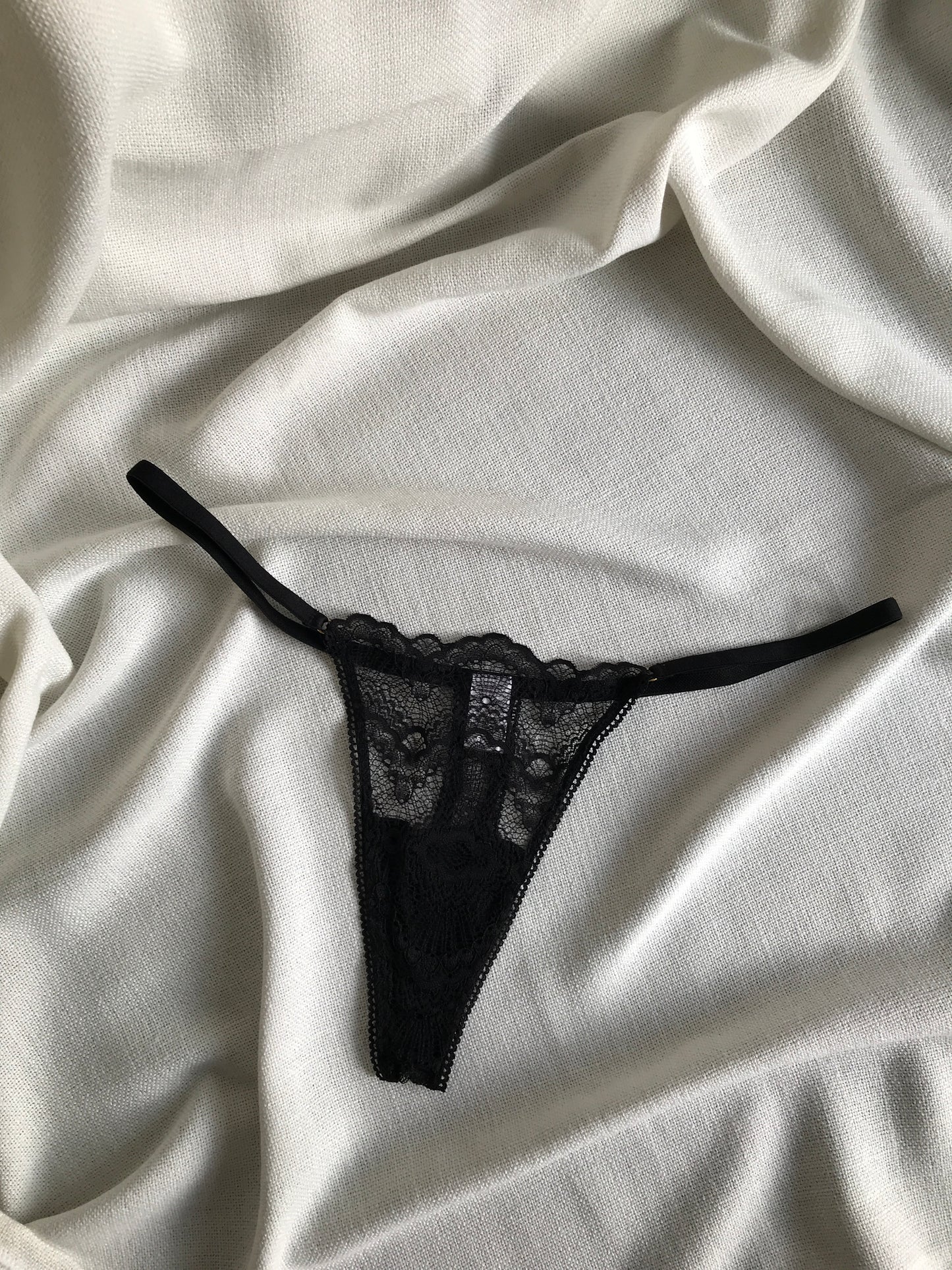 A black lace g-string underwear on a white silky surface.