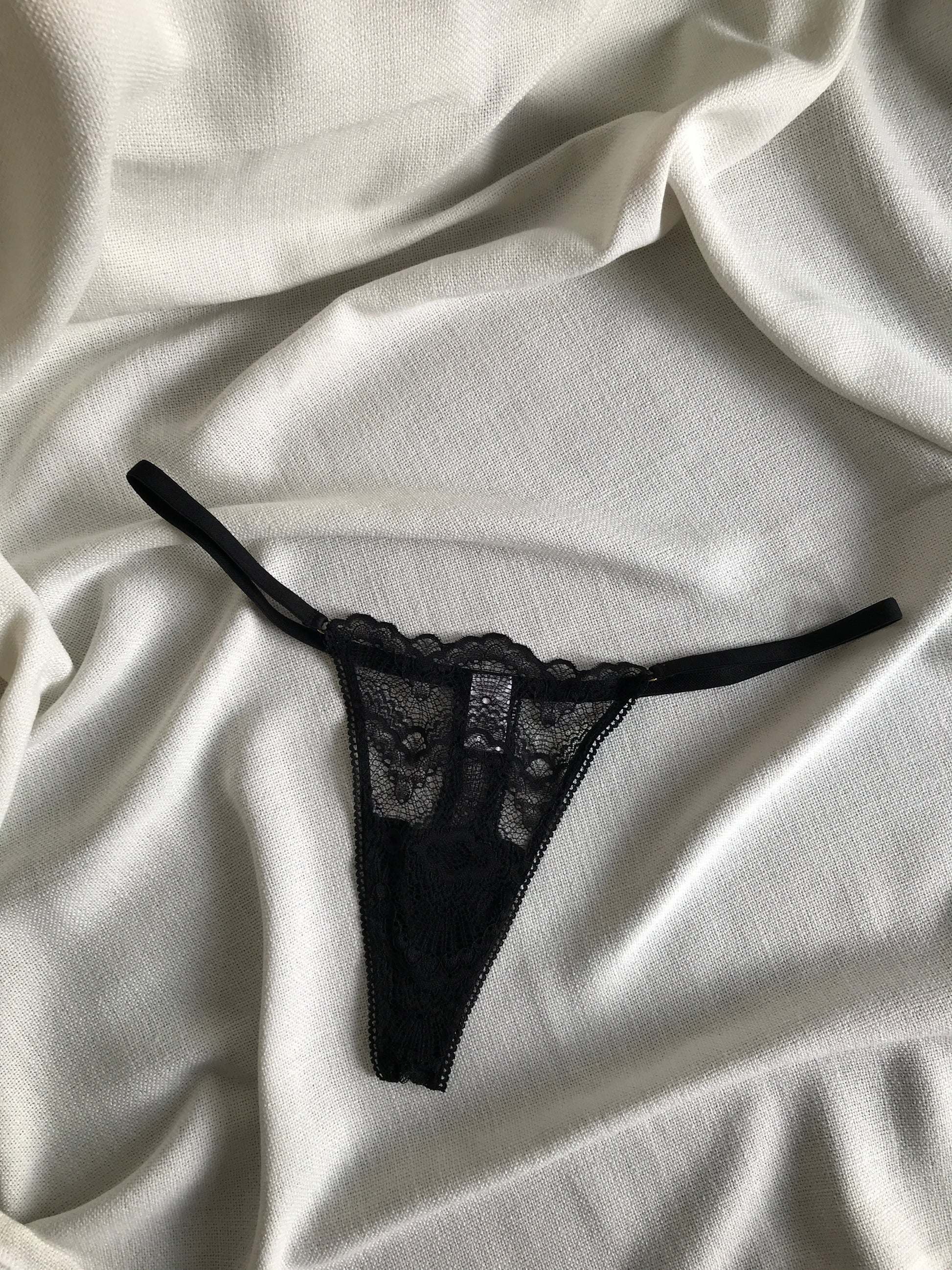 A black lace g-string underwear on a white silky surface.