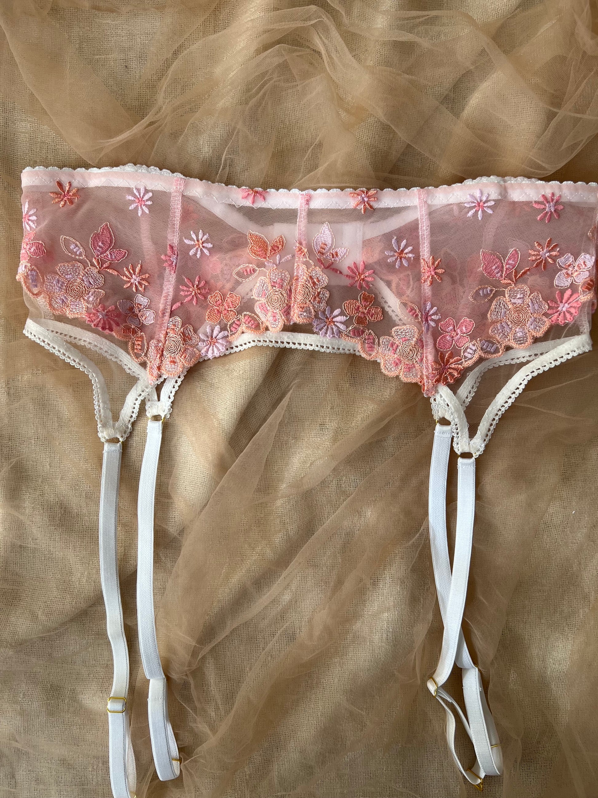Pink lace garter belt with floral embroidery on a beige fabric background